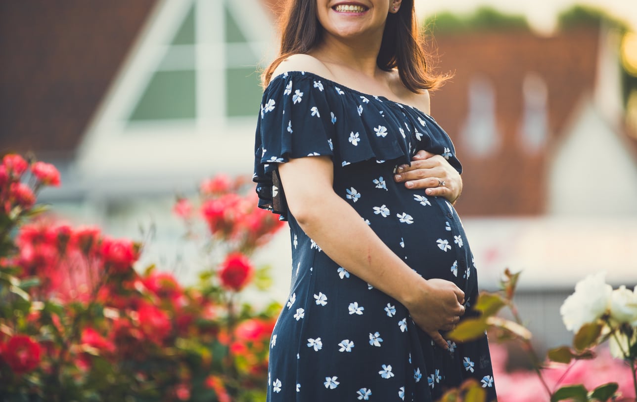 Happy pregnant woman standing by flowers