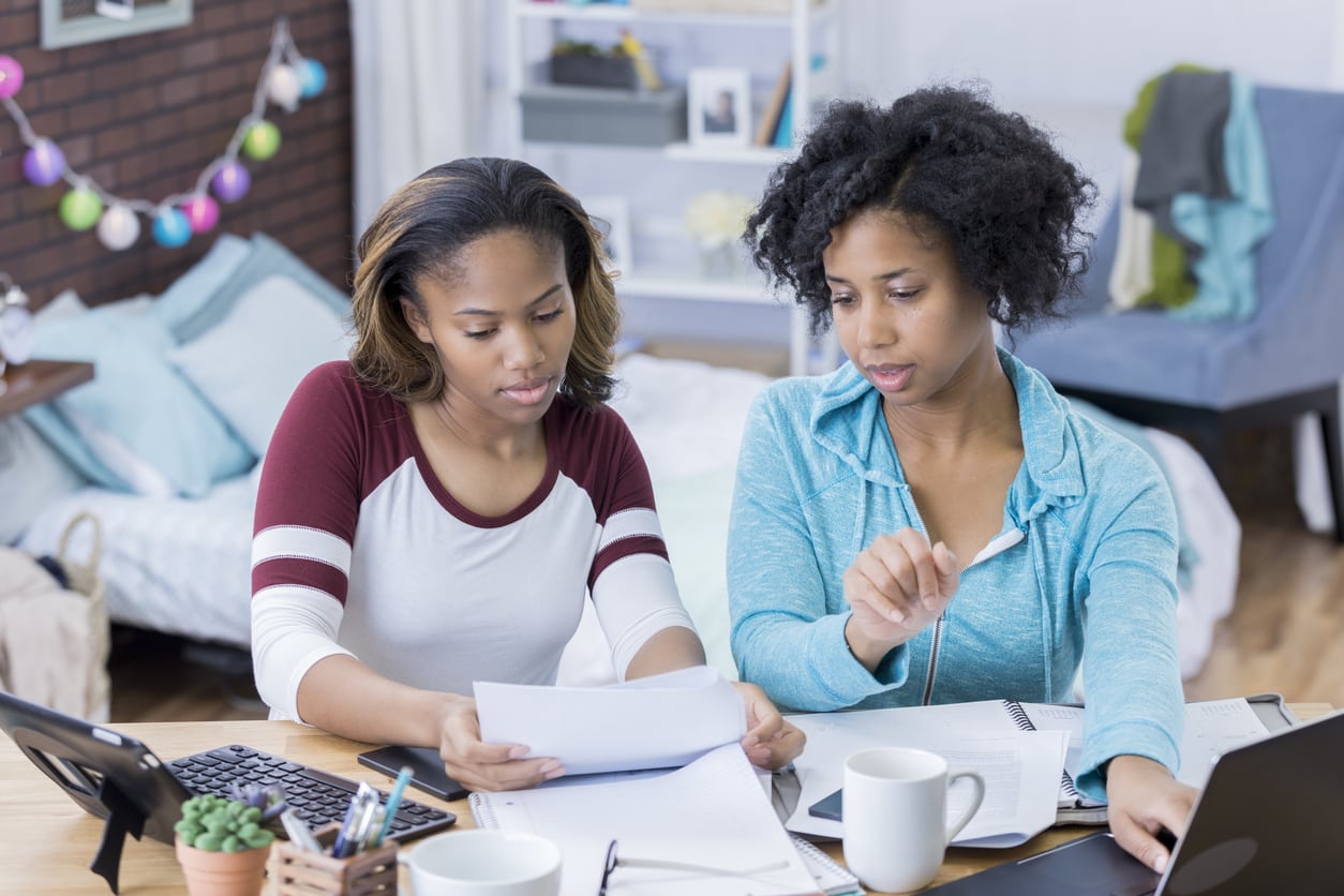 Young woman and mid adult woman work on a paper in a college dorm.