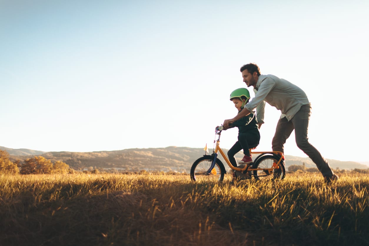 Father teaching son how to ride a bike in an open field