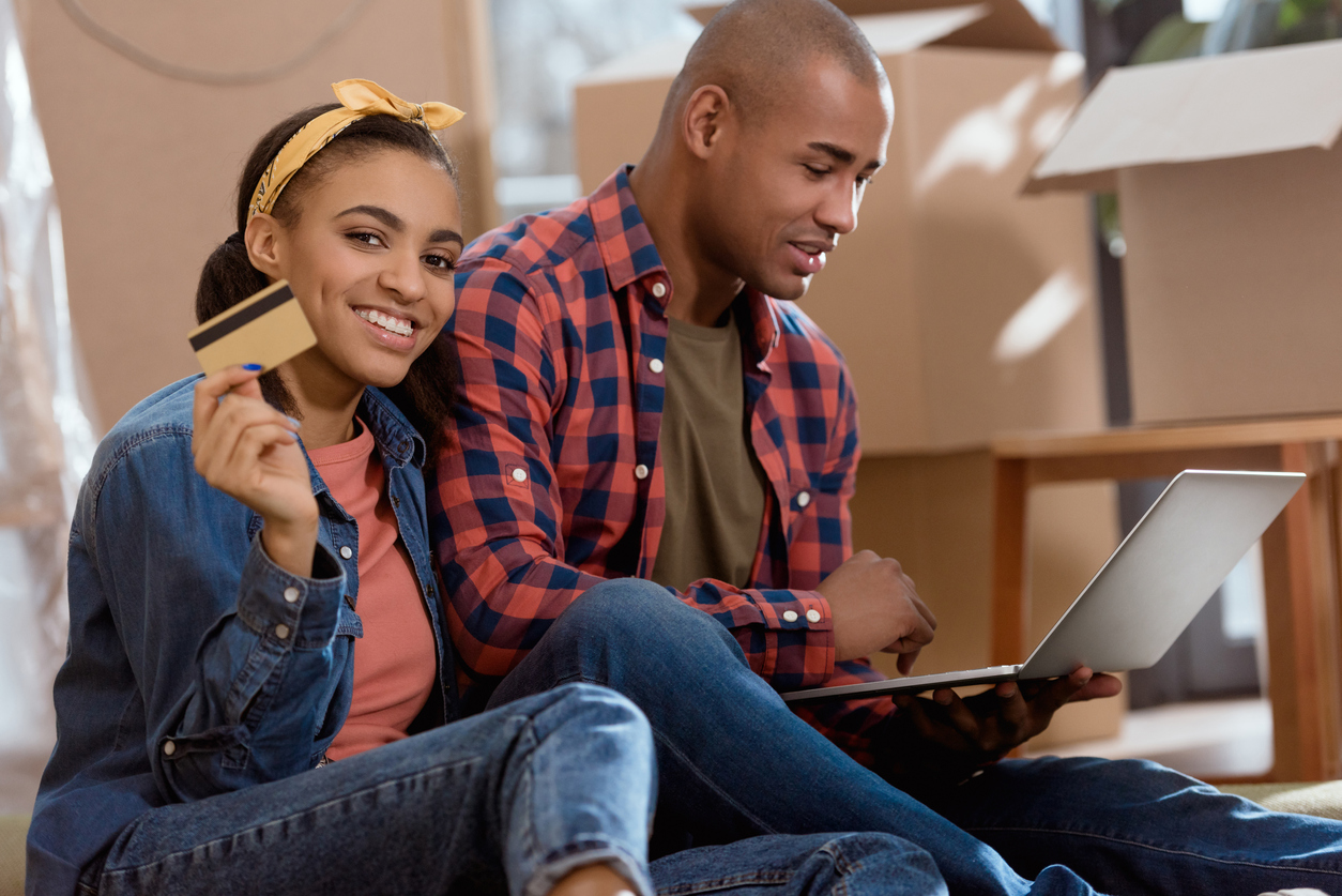 Two people shopping online with credit card and laptop in new apartment