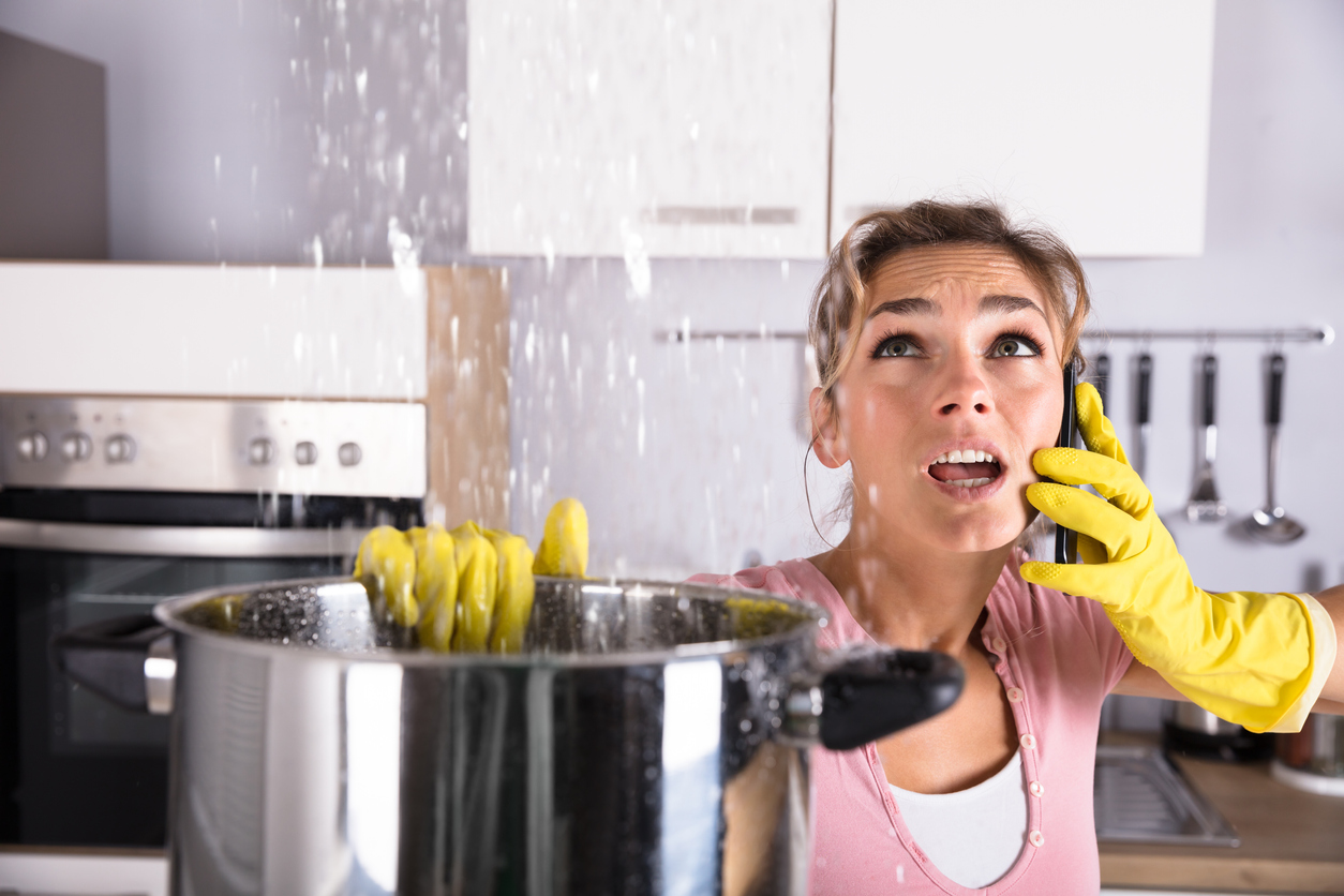 Stressed woman with pot in her hand catching water from a leaking ceiling