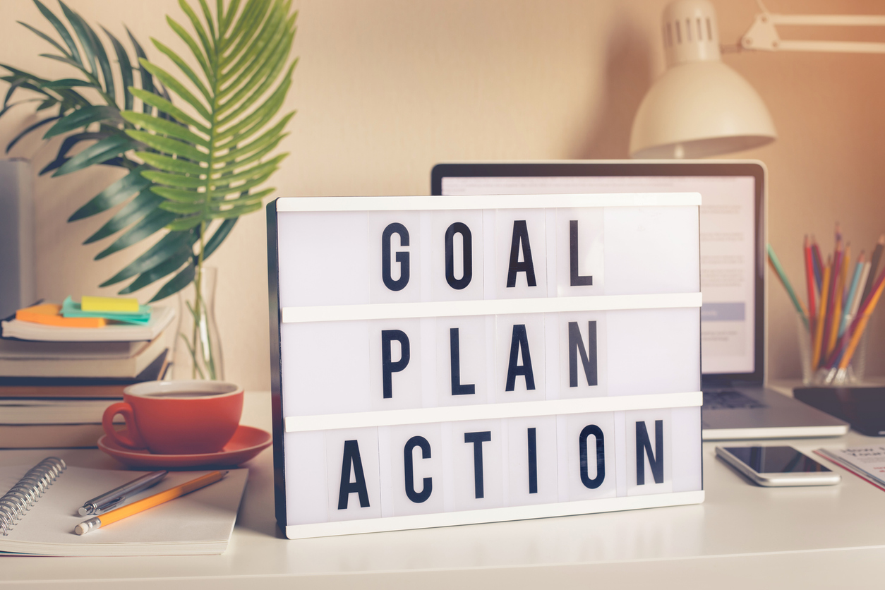 A desk with a laptop, coffee, and a sign that says goal, plan, action on it